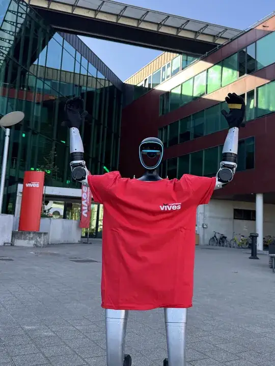 Humanoider Roboter im roten Shirt der Hogeschool VIVES mit erhobenen Armen vor dem Campus